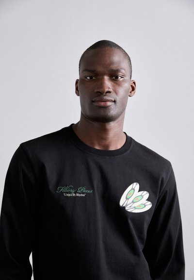 Black long-sleeve T-shirt made of cotton, featuring a graphic design with white and green accents on the left chest. Text reads "Filling Pieces."