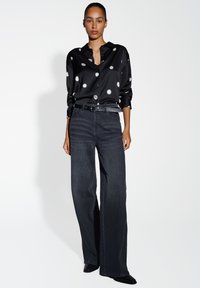Black satin shirt with white polka dots, long sleeves, and collar, paired with high-waisted dark denim wide-leg jeans and black heels.