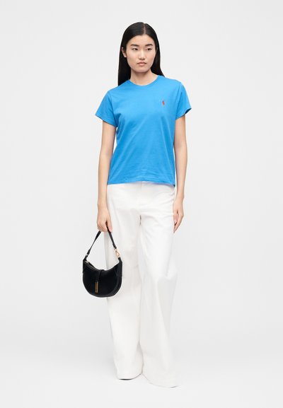 Mėlynas medvilninis trumpomis rankovėmis marškinėlis su raudonu logotipu, derinamas su baltomis plačiomis kelnėmis. Juoda rankinė su išlenkta forma ir auksiniu akcentu.