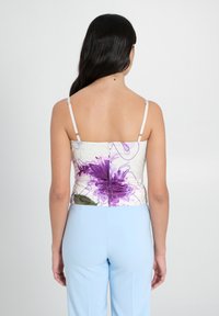 Top bianco con stampa floreale viola, spalline sottili e design aderente. Abbinato a pantaloni su misura di un leggero blu. Tessuto dalla texture liscia.