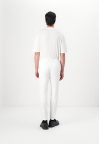 Weißes T-Shirt mit kurzen Ärmeln, kombiniert mit weißen Slim-Fit-Hosen mit glatter Textur und minimalistischem Design. Schwarze Schuhe runden den Look ab.