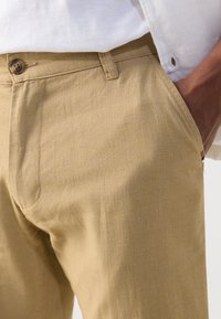 Beige linased püksid tekstuurse viimistluse ja nööbiga kinnitusega, vööaugete ja küljetaskutega. Minimalistlik disain, sobiv lõige.