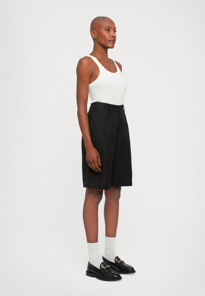 Svart skreddersydde shorts laget av lett stoff, med høy midje og løs passform. Kombinert med en hvit tank top og svarte loafers.