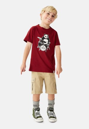 Vinrød T-shirt med panda- og trommeillustration, kombineret med khaki cargoshorts. Olivengrønne sneakers med hvide såler og grå mønstrede sokker.