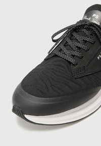 Černá atletická obuv s texturovaným textilním svrškem, zesílenou gumovou špičkou, plochými černými tkaničkami a nenápadným logem na jazyku.