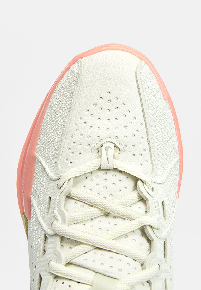 Zapatilla deportiva ligera con un empeine texturizado en blanco roto, suela de goma rosa y acentos perforados; cuenta con cordones y un logo de marca.
