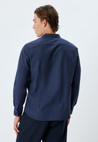 Marineblaue Langarmbluse mit strukturiertem Muster, geknöpften Manschetten und klassischem Kragen-Design. Verfügt über eine taillierte Passform und Detail am Rücken.