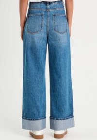 Jeans de mezclilla azul de pierna ancha con cintura alta, puños doblados y dos bolsillos traseros. Textura suave con un lavado desgastado.