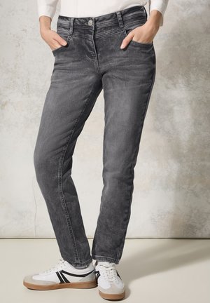 Harmaat denim-farkut kapealla leikkauksella, viisi taskua, nappikiinnitys ja hienovaraisia haalistumisdetaileja. Yhdistetty valkoisiin tennareihin, joissa on mustia yksityiskohtia.