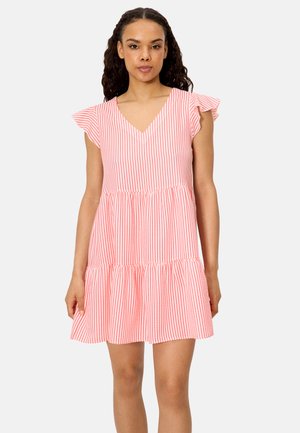 Mujer con vestido corto a rayas verticales rosas y blancas, con mangas cortas con volantes y falda de capas, de pie contra un fondo liso.