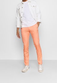 Pantaloni leggeri color pesca con una vestibilità slim, abbinati a una t-shirt bianca e a una giacca di denim bianca. Calzature casual completano il look.