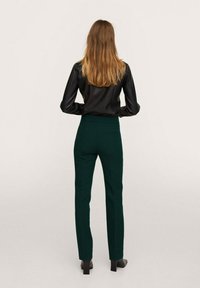 Chemise noire en satin à manches longues associée à un pantalon ajusté vert foncé. Le pantalon a une taille haute et un design épuré.