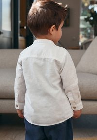 Camicia di lino bianco con polsino abbottonato, caratterizzata da un colletto classico e un orlo curvo, abbinata a pantaloni blu navy.