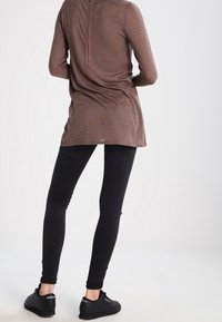 Braunes Langarmoberteil mit einem Reißverschluss am Kragen, kombiniert mit schwarzen Leggings und schwarzen Sneakers, mit einer glatten Textur und angepasstem Design.