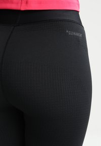 Leggings deportivos negros con un tejido texturizado, cintura alta y un logotipo sutil en gris cerca de la parte superior de la espalda.