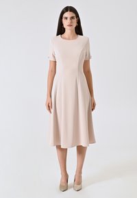 Ein knie-langes, hellrosa Kleid mit kurzen Ärmeln, einem runden Halsausschnitt und einem ausgestellten Rock; texturiertem Stoff mit glatter Oberfläche.