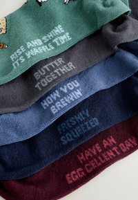 Cinq paires de chaussettes de couleurs variées : vert, gris, bleu, marine et bordeaux, chacune arborant un texte unique dans des couleurs de fil contrastantes.