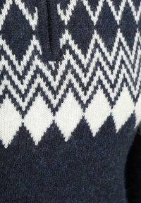 Dunkelblauer Strickpullover mit weißen Zickzack- und Rautenmuster über der Brust sowie strukturiertem Wollstoff.