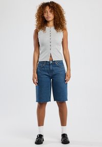 Gray sleeveless top with a button front, paired with knee-length blue denim shorts. White socks and black slip-on shoes complete the look.