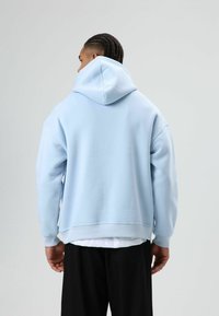 Sweat à capuche bleu clair avec une grande capuche, des poignets côtelés et une coupe décontractée. Le tissu semble doux avec une texture lisse.