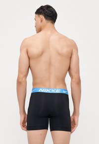 Čierne športové boxerky s svetlomodrým pásom s logom "NIKE"; hladká textúra, tesný strih a dĺžka do polovice stehien.