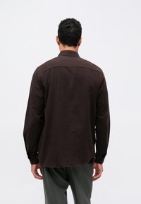 Camicia marrone a maniche lunghe realizzata in tessuto morbido, con colletto classico, polsini con bottoni e taglio dritto all'orlo.