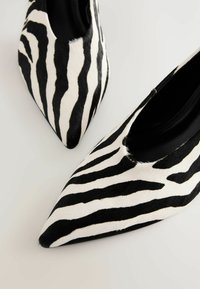 Black and white pointed-toe flats with a zebra pattern, made of sleek hair-on-hide material, featuring a smooth interior and minimalistic design.