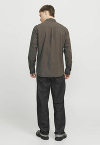 Camisa de botones gris oscuro con mangas largas, canesú en la parte posterior y dobladillo redondeado, usada con jeans de mezclilla oscuros y zapatos negros.