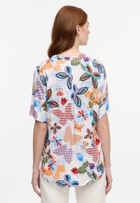 Kortærmet bluse med et livligt blomster- og sommerfuglemønster. Fremstillet af letvægtsstof med rund halsudskæring og afslappet pasform.