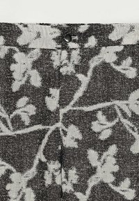 Tissu noir et gris avec un motif floral, présentant un tissage texturé, une fermeture à bouton et des détails subtils en contraste.