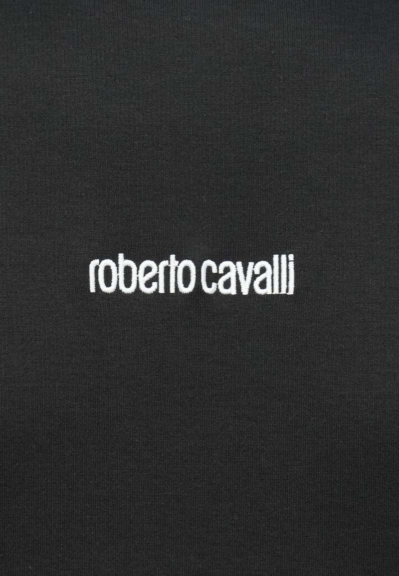 Tissu noir avec un logo "roberto cavalli" brodé en blanc, centré dessus.