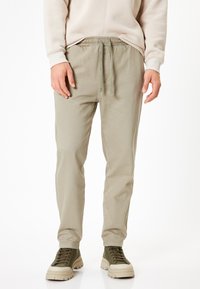 Lyse olivenfarvede bomuldsblandede joggers med elastisk talje og snøre. Glat tekstur, tapered ben og synlige sidelommer.