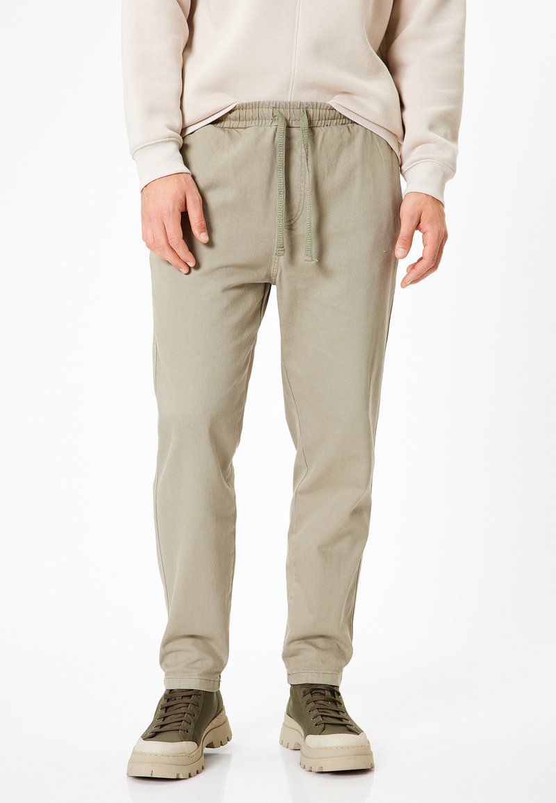 Lyse olivenfarvede bomuldsblandede joggers med elastisk talje og snøre. Glat tekstur, tapered ben og synlige sidelommer.