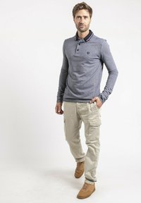 Polo gris à manches longues avec un col sombre et une rayure rouge, associé à un pantalon cargo en khaki et des chaussures brunes. Tenue décontractée avec une coupe relax.