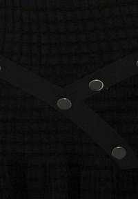 Tissu noir texturé avec des sangles noires superposées maintenues par six boutons-pression métalliques en motif diagonal.