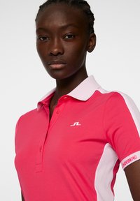 Rosa polo skjorta med vit krage, en liten logotyp på bröstet och randiga designelement längs axlarna och ärmarna.