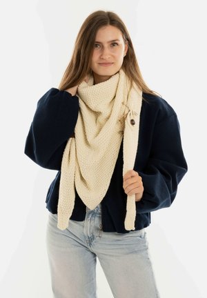 Knitted cream scarf draped around the neck, textured pattern, paired with a navy jacket. Features a wooden toggle and knotted accent.