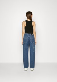 Top preto sem mangas combinado com calças cargo de denim azul folgadas, apresentando grandes bolsos laterais e um silhueta descontraída.