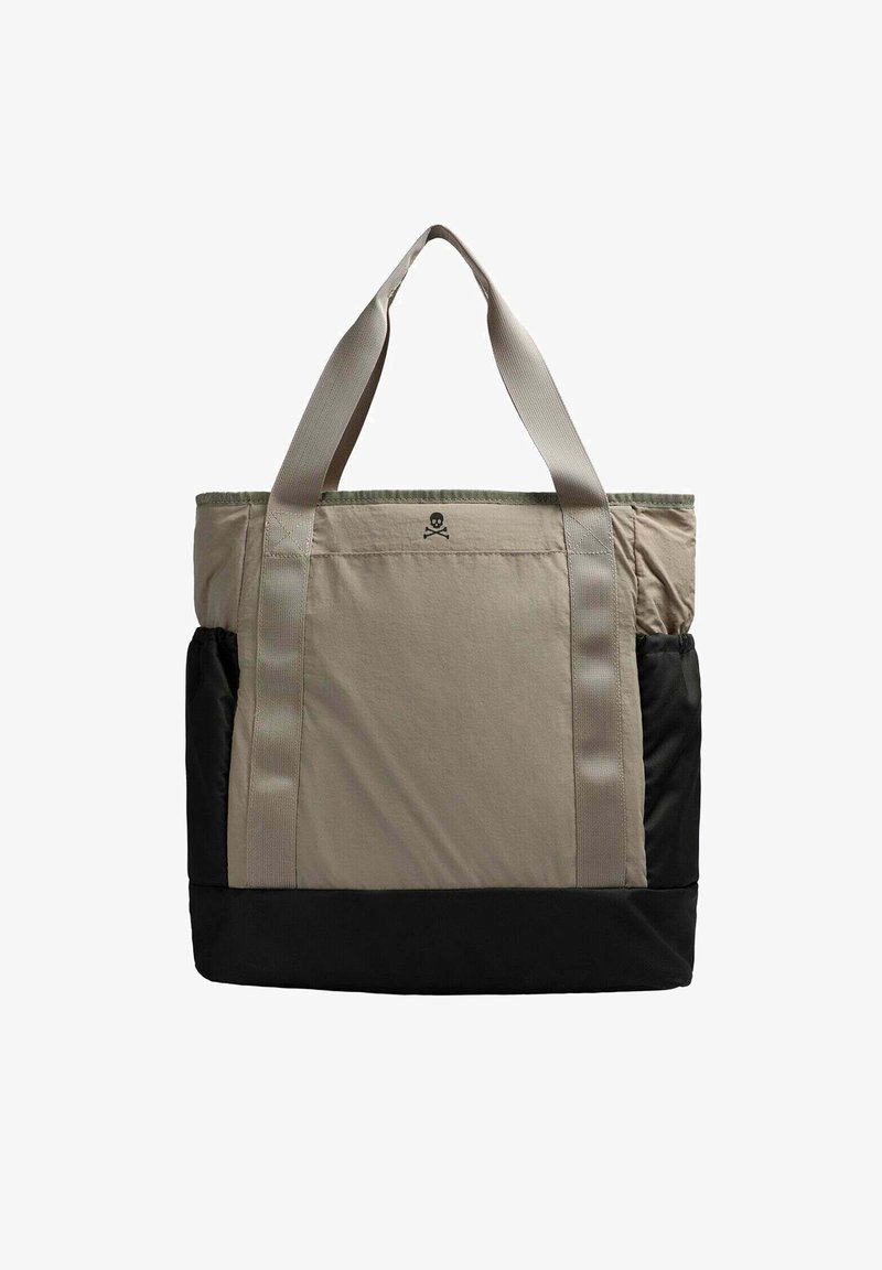 Bolso tote en beige y negro, con un gran compartimento principal, dos asas de transporte y un pequeño logo de calavera en la parte frontal.