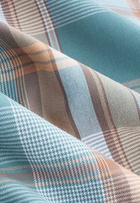 Tessuto intrecciato con motivo a quadri nei colori turchese, beige e marrone. Superficie strutturata con spessori di filo variabili.