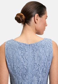 Robe sans manches bleu clair avec des détails en dentelle intriqués et une fermeture éclair dans le dos, mettant en valeur des motifs floraux et un tissu texturé.