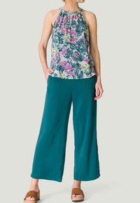 Haut à bretelles fleuri en blanc, rose et vert associé à un pantalon large teal et des sandales à plateforme marron. Tissu léger, coupe décontractée.