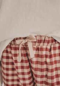 Rot- und cremefarbene karierte Shorts mit einem elastischen Bund und einem gebundenen Bändchendetail an der Vorderseite. Der Stoff wirkt weich und leicht.