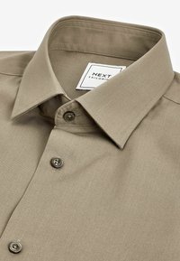 Beige op maat gemaakte blouse met een zachte textuur, een gespreide kraag en drie grijze knopen op de sluiting; het label zegt "NEXT TAILORING."