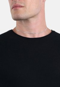 Collana choker in argento su collo nudo, caratterizzata da una catena sottile e liscia con un design minimalista. Indossata con una maglietta nera a girocollo.