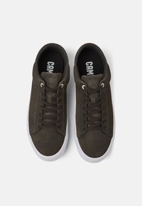 Baskets en daim vert foncé avec des lacets marron, semelles en caoutchouc blanc et un logo sur la semelle intérieure noire. Bout arrondi et design décontracté à tige basse.