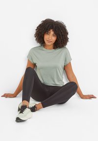 Light green short-sleeve t-shirt paired with black leggings. The t-shirt features a relaxed fit. Model wears light sneakers with dark accents.