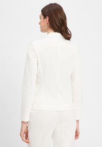 Witte tailoring blazer met lange mouwen en ingeknipte kraag, voorzien van een soepele textuur en een getailleerde pasvorm. De achterkant laat schone lijnen zien.