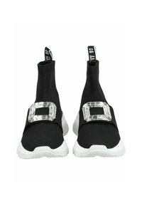 Des baskets slip-on en tissu noir avec une épaisse semelle blanche, présentant un grand accent de boucle claire à l'avant. Côtés texturés et languettes de tirage.