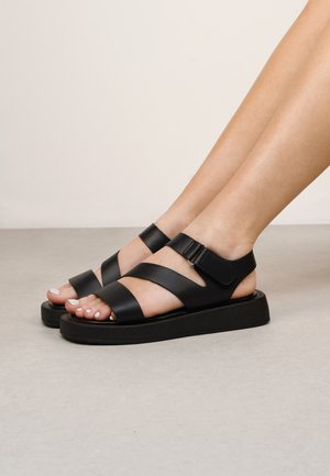 Sandalias negras con correas anchas mate, hebilla ajustable y suela de plataforma gruesa. Textura suave con diseño de punta abierta.